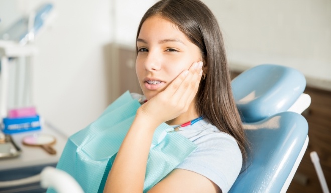 Young woman holding her cheek in pain while visiting emergency dentist in San Marcos