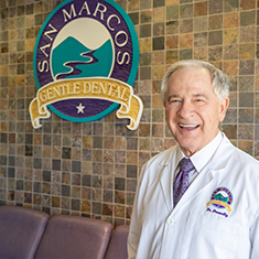 Doctor Donnelly smiling next to sign on wall that reads San Marcos Gentle Dental