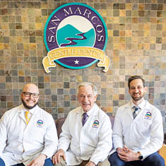 Three dentists sitting on bench with San Marcos Gentle Dental sign on wall behind them