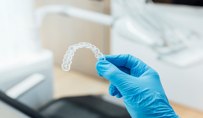 Smiling blonde woman holding an Invisalign aligner
