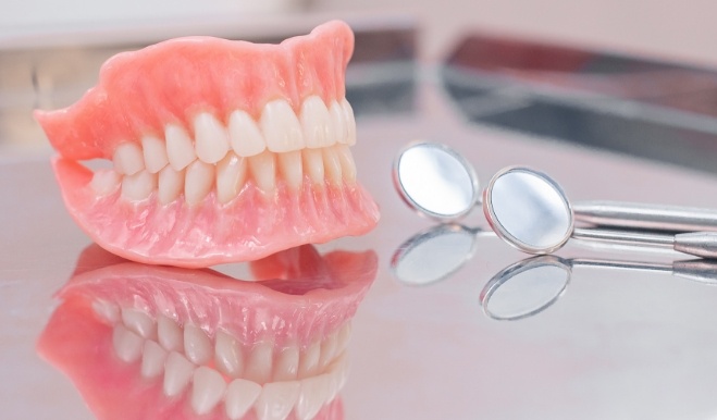 Full dentures on table next to two dental mirrors