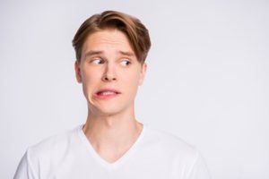 Man wearing a white v-neck top in front of a light grey background with a worried look on his face