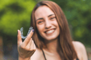 Woman holding an Invisalign tray with trees in the background