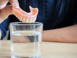 Patient dropping their dentures in a cleaning solution