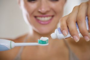 woman putting toothpaste on an electric toothbrush 